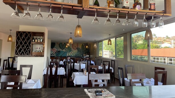 A restaurant interior with a wine rack, hanging lights, and a mural on the wall. - Arcadia Suites (Kampala)