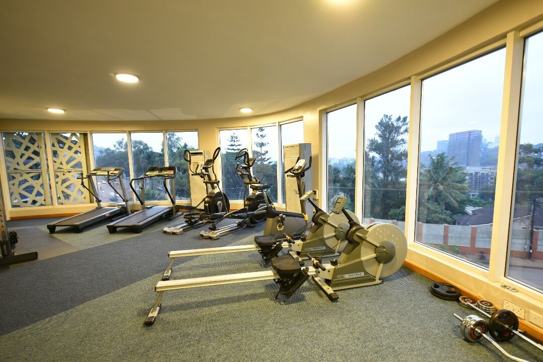 A gym with treadmills, elliptical machines, and weight equipment, large windows with a city view.