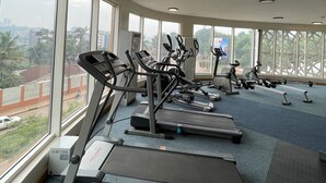 A gym with various exercise equipment, large windows, and a view of the city. - Arcadia Suites (Kampala)
