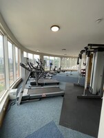 Un gimnasio con cintas de correr, elípticas y equipos de pesas, ventanas amplias y suelo alfombrado.