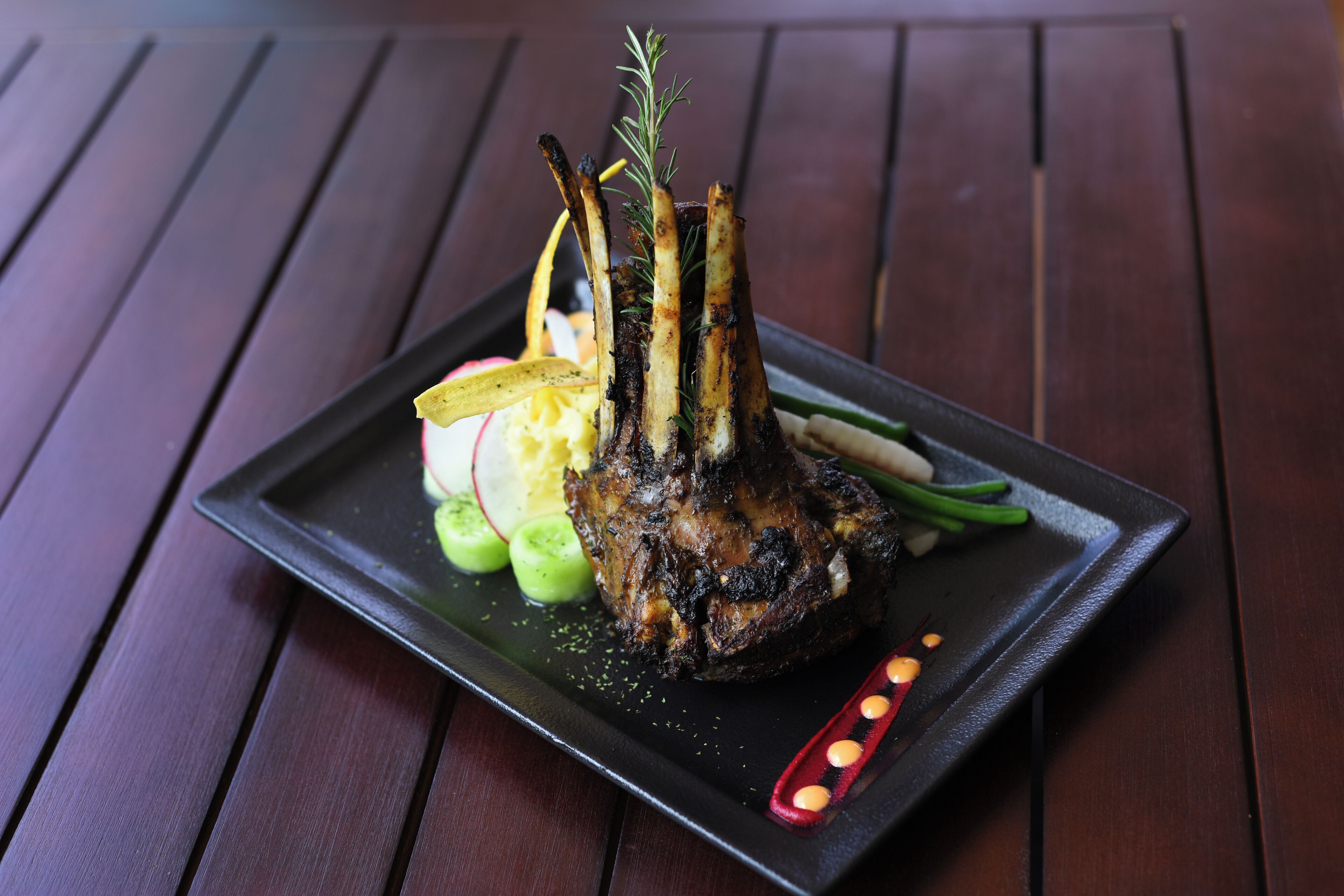 A plate with a roasted meat dish, garnished with herbs, accompanied by sliced vegetables.