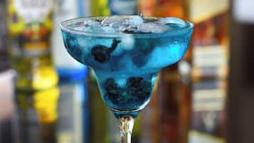 Een cocktail in een glas met ijsblokjes en een muntblaadje, met wazige flessen op de achtergrond.