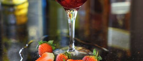 Un verre à cocktail garni de fraises et d’une branche de romarin, posé sur un sous-verre noir.