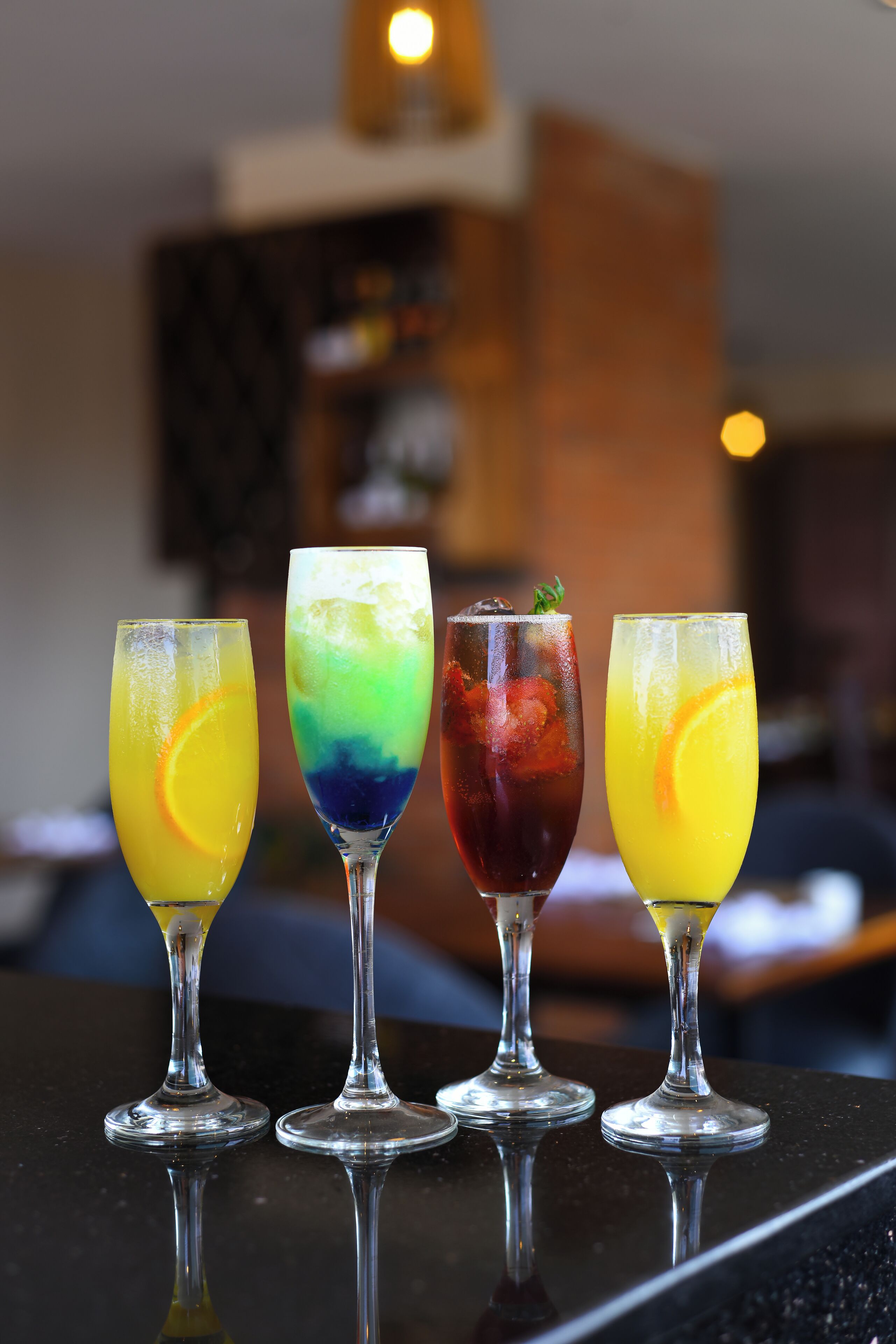 Four glasses of colorful cocktails on a reflective surface.