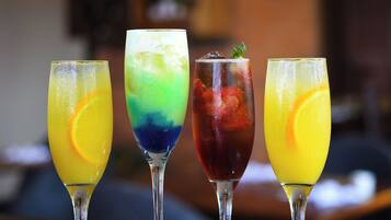 Four glasses of colorful cocktails on a reflective surface.