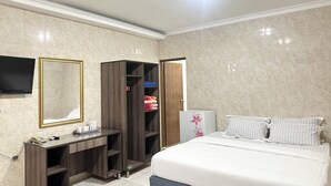 Una habitación de hotel con cama, escritorio con silla, armario, televisor y espejo.