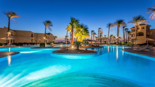 A large swimming pool with multiple sections, surrounded by palm trees and lounge chairs.