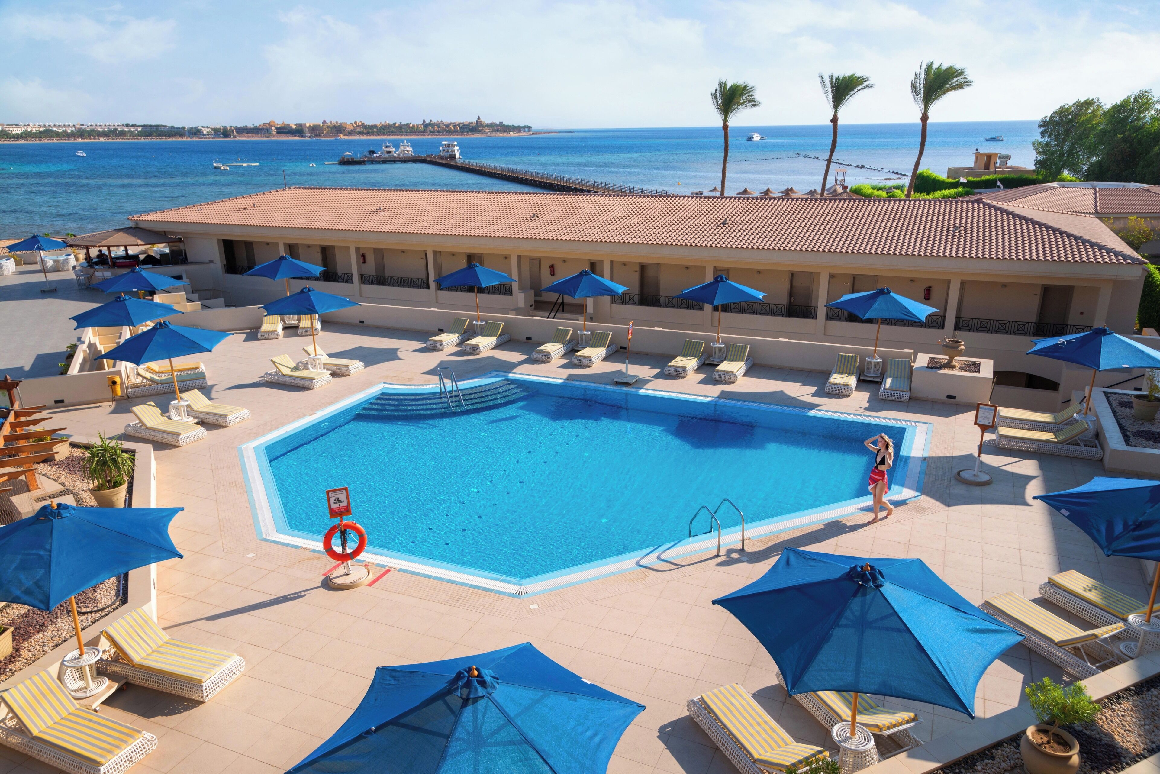 Zwembad van een resort met ligbedden en parasols, een helder uitzicht op de oceaan en een rederspost.