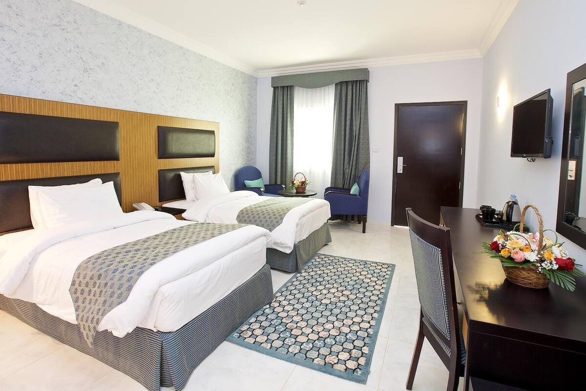 A hotel room with two beds, a desk, a chair, a TV, and a door.