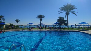 Une piscine à l’eau cristalline, entourée de palmiers et ombragée par des parasols bleus.