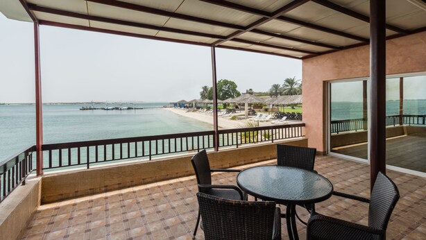 Un espace extérieur abrité, équipé d’une table et de chaises, offrant une vue sur une plage et la mer.