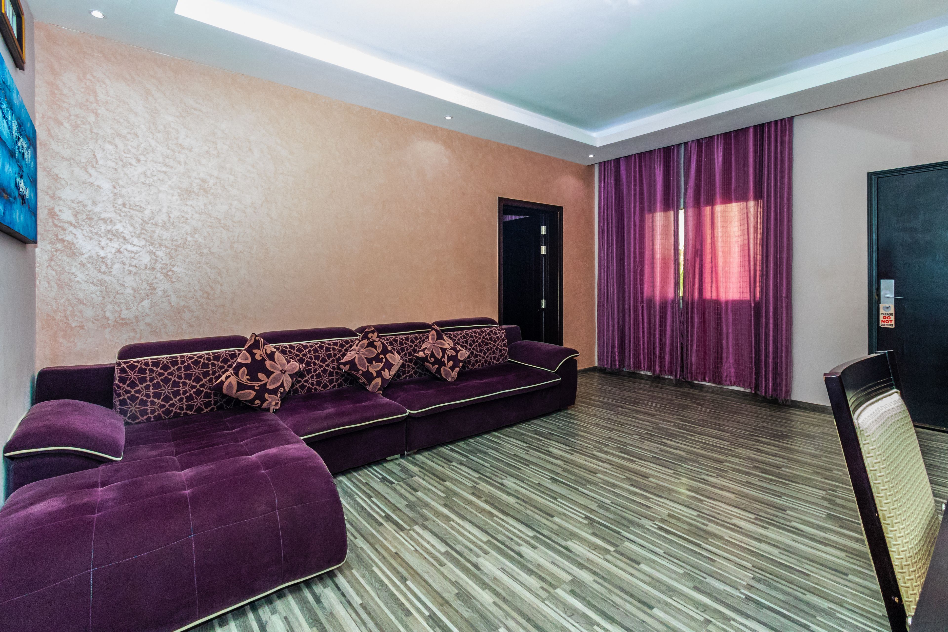 Una habitación moderna con un sofá modular púrpura, una puerta y una ventana con cortinas moradas.