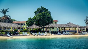 Un complexe hôtelier situé en bord de mer, doté de parasols en chaume, de chaises longues et offrant une vue dégagée sur l’océan.