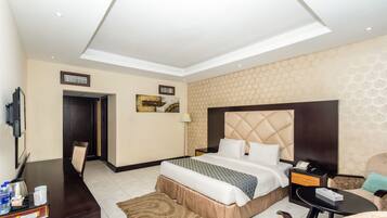 A hotel room with a bed, a desk, a chair, a TV, and a wall-mounted artwork.