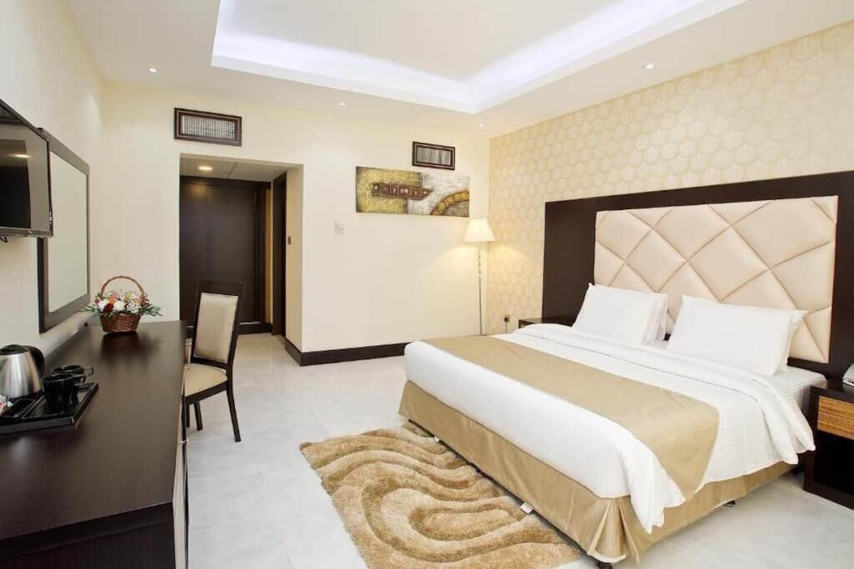 A hotel room with a bed, bedside table, lamp, and a view of the hallway.