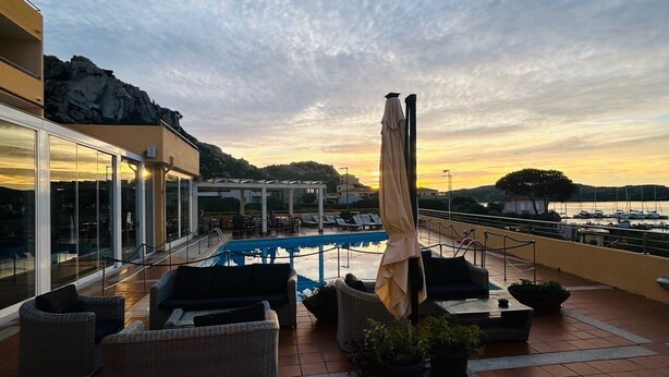 A rooftop terrace with a swimming pool, outdoor seating, and a view of the sunset over the water.