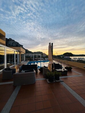 Una terraza en la azotea con piscina, mobiliario exterior y vistas al atardecer sobre el agua.