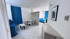 A modern, well-lit room with a dining table, chairs, a sofa, and a bed.