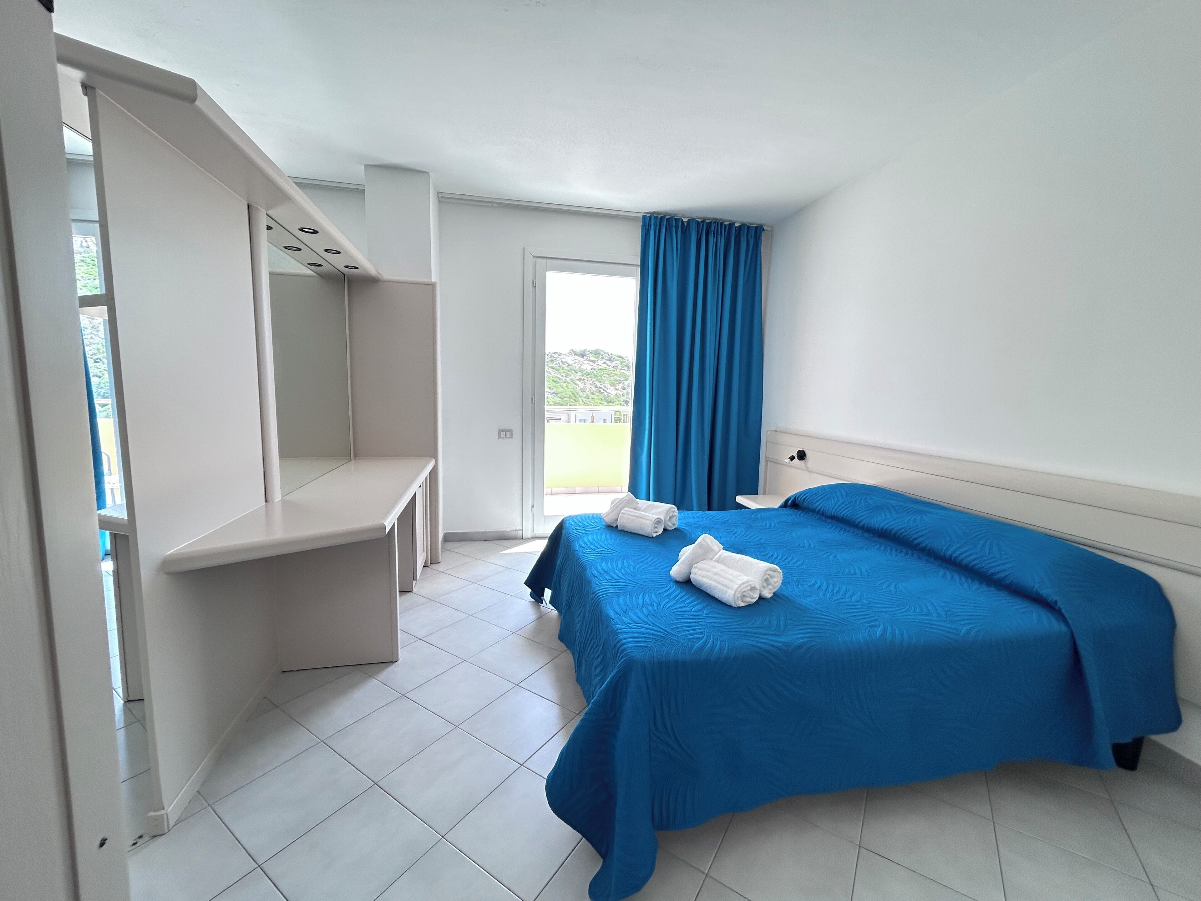 A bedroom with a bed, a desk, and a window with curtains.