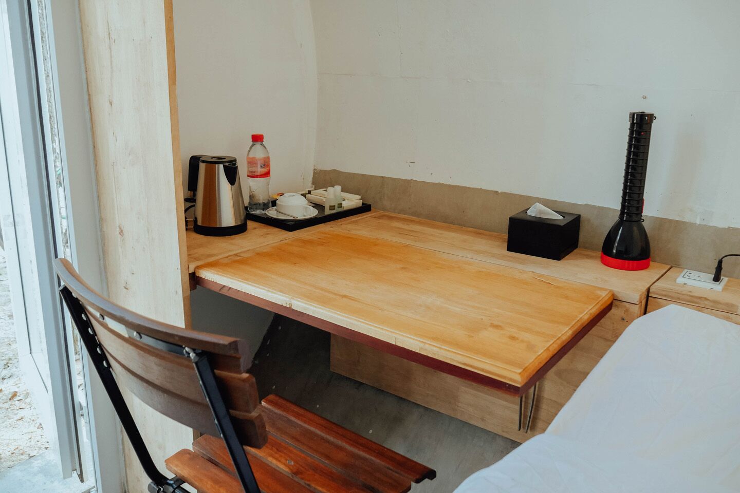 Une petite cuisine équipée d’un plan de travail en bois, d’une bouilloire, d’une bouteille d’eau, d’une boîte de mouchoirs et d’une lampe rouge et noire.