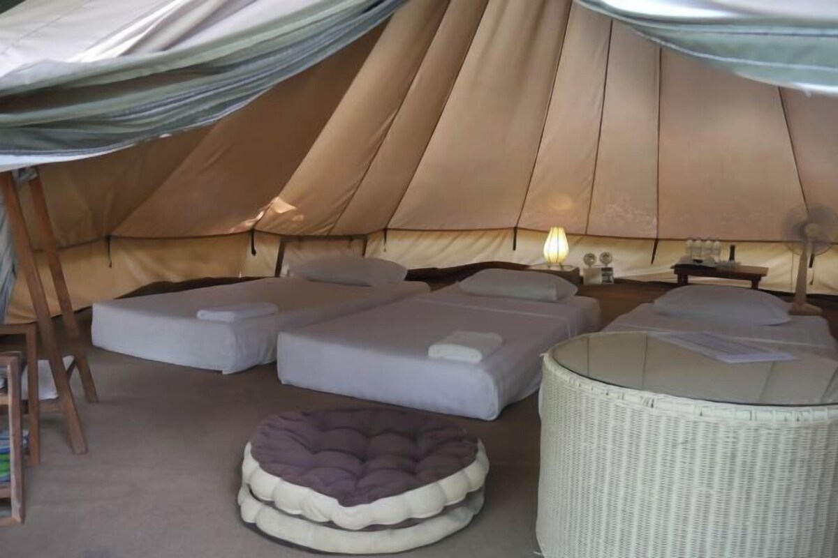 Una carpa con tres camas, una mesita con una lámpara y una silla de mimbre.