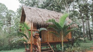Una cabaña de madera rústica con techo de paja, rodeada de exuberante follaje y palmeras.