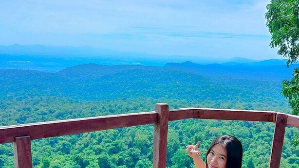 Una persona sentada en una plataforma de madera con vistas a un bosque verde y exuberante y montañas a la distancia.