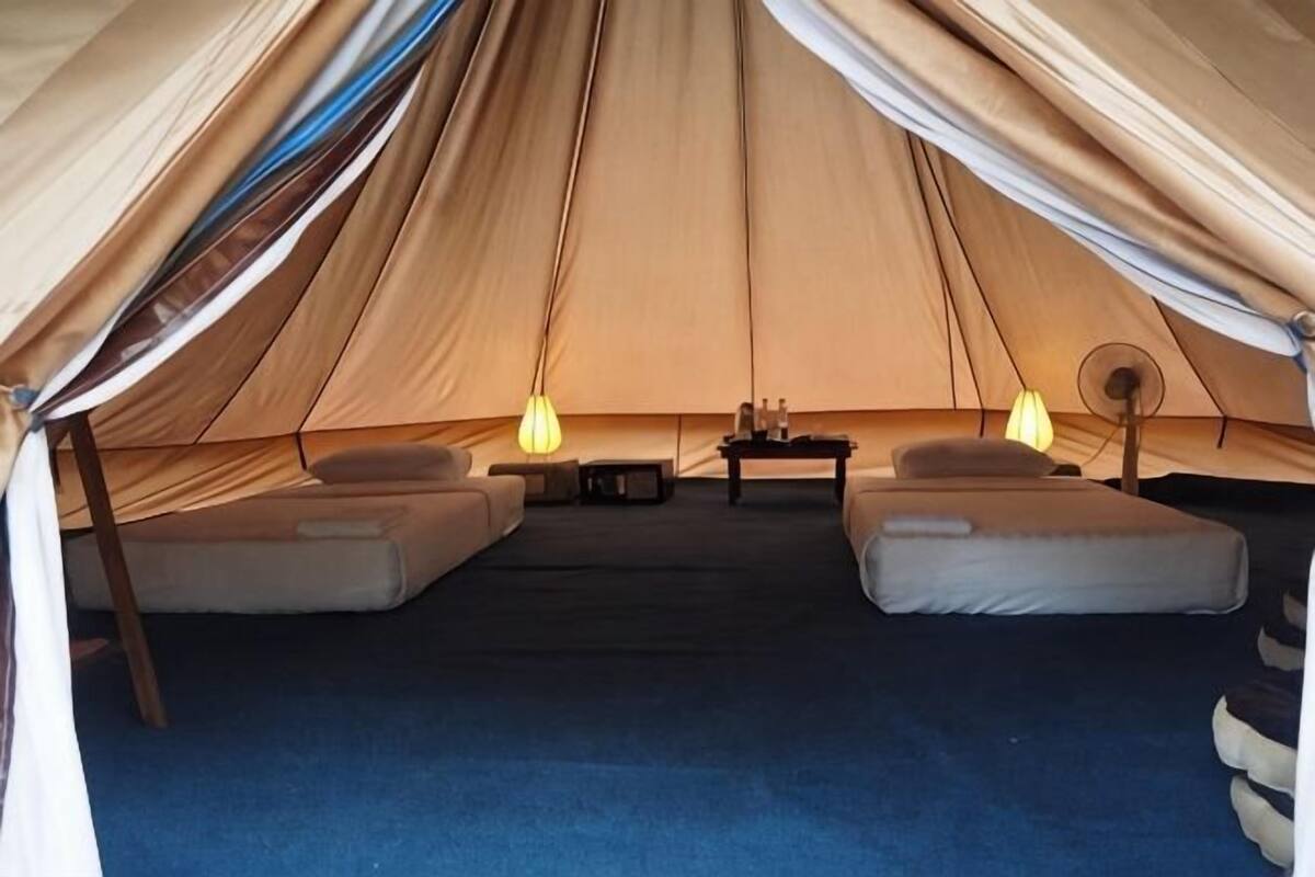 Una carpa con dos camas, una mesa y dos lámparas.