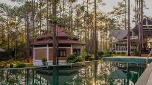 Un área de piscina tranquila con un pabellón y un edificio rodeado de árboles altos.