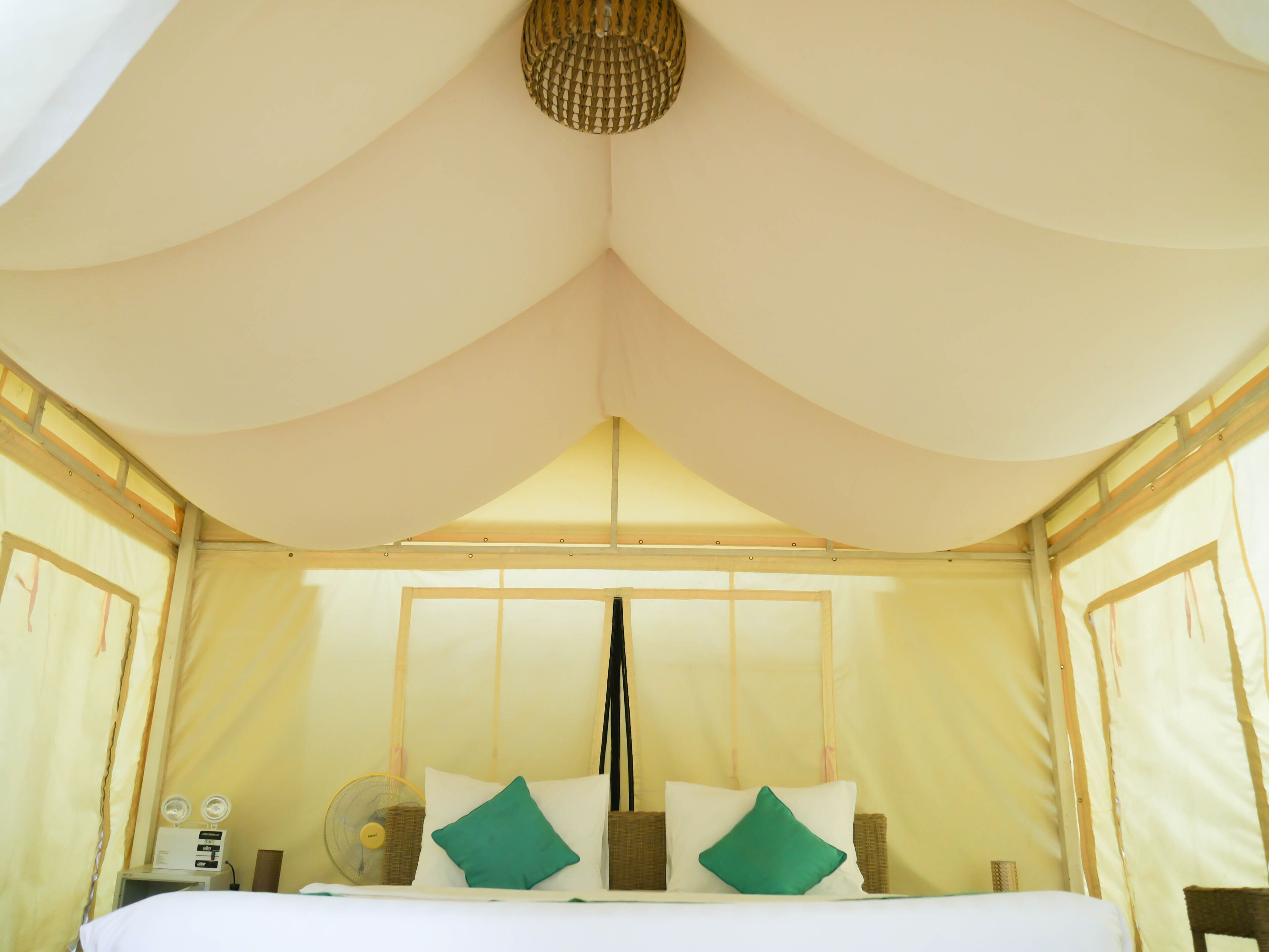 A tent-style bedroom with a bed, pillows, a fan, and a small table with a lamp.