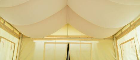 A tent-style bedroom with a bed, pillows, a fan, and a small table with a lamp.