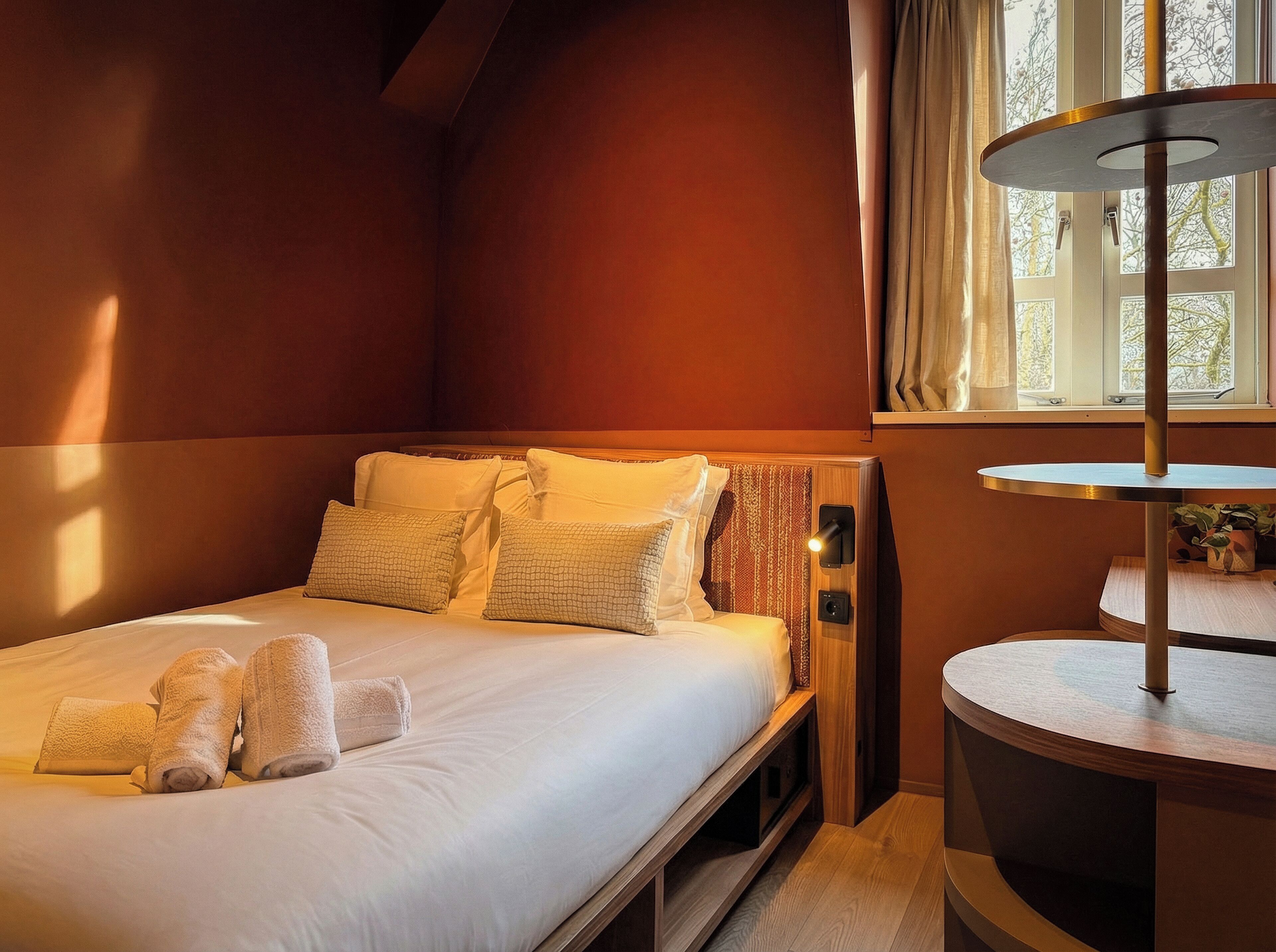 Een hotelkamer met een bed, nachtkastje, lamp en raam met gordijnen.