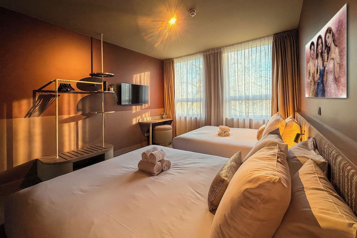 Ett hotellrum med två sängar, en tv, ett skrivbord och en tavla på väggen.