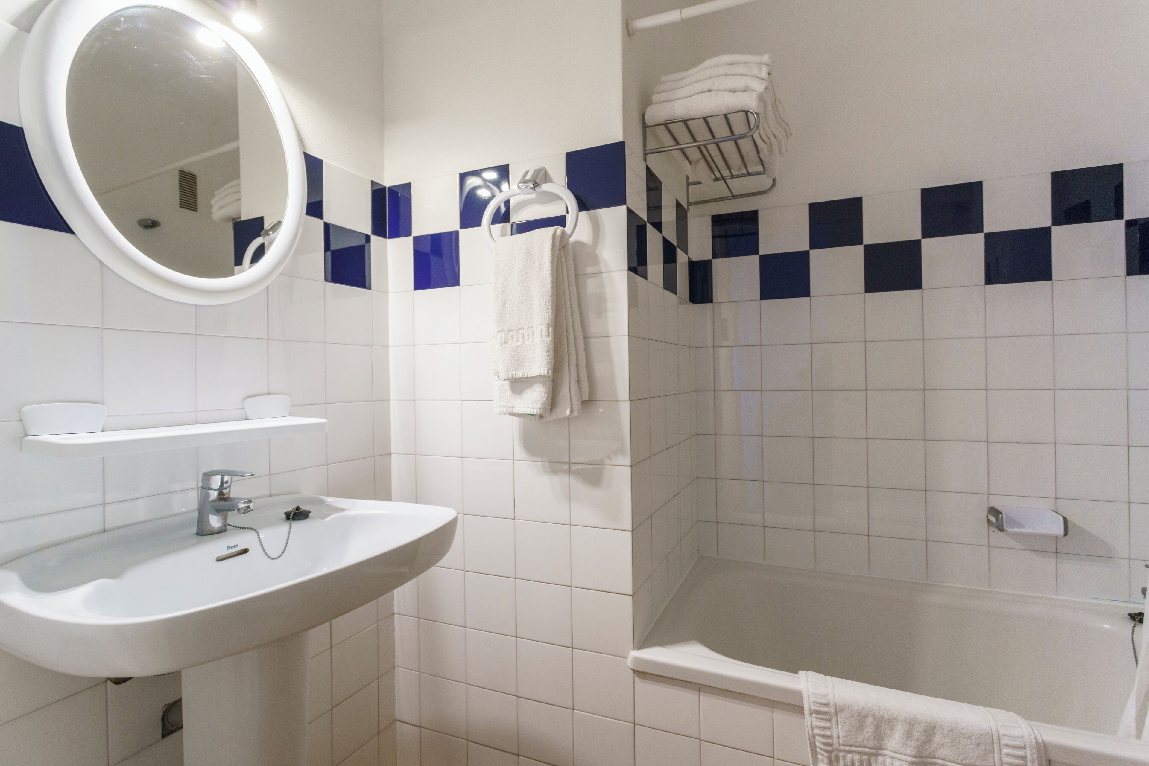 A bathroom with a sink, mirror, towel rack, and a bathtub.