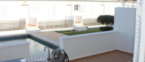 Un pequeño espacio al aire libre con piscina, una mesa con sillas y un edificio blanco al fondo.