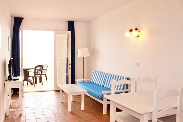 A room with a sofa, a table, a chair, a lamp, and a view through an open door.
