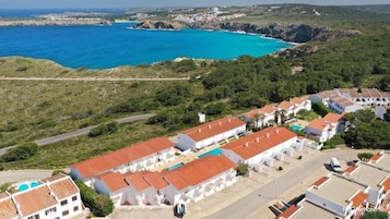 Uma vila costeira com edifícios brancos, uma piscina e vista para o mar.