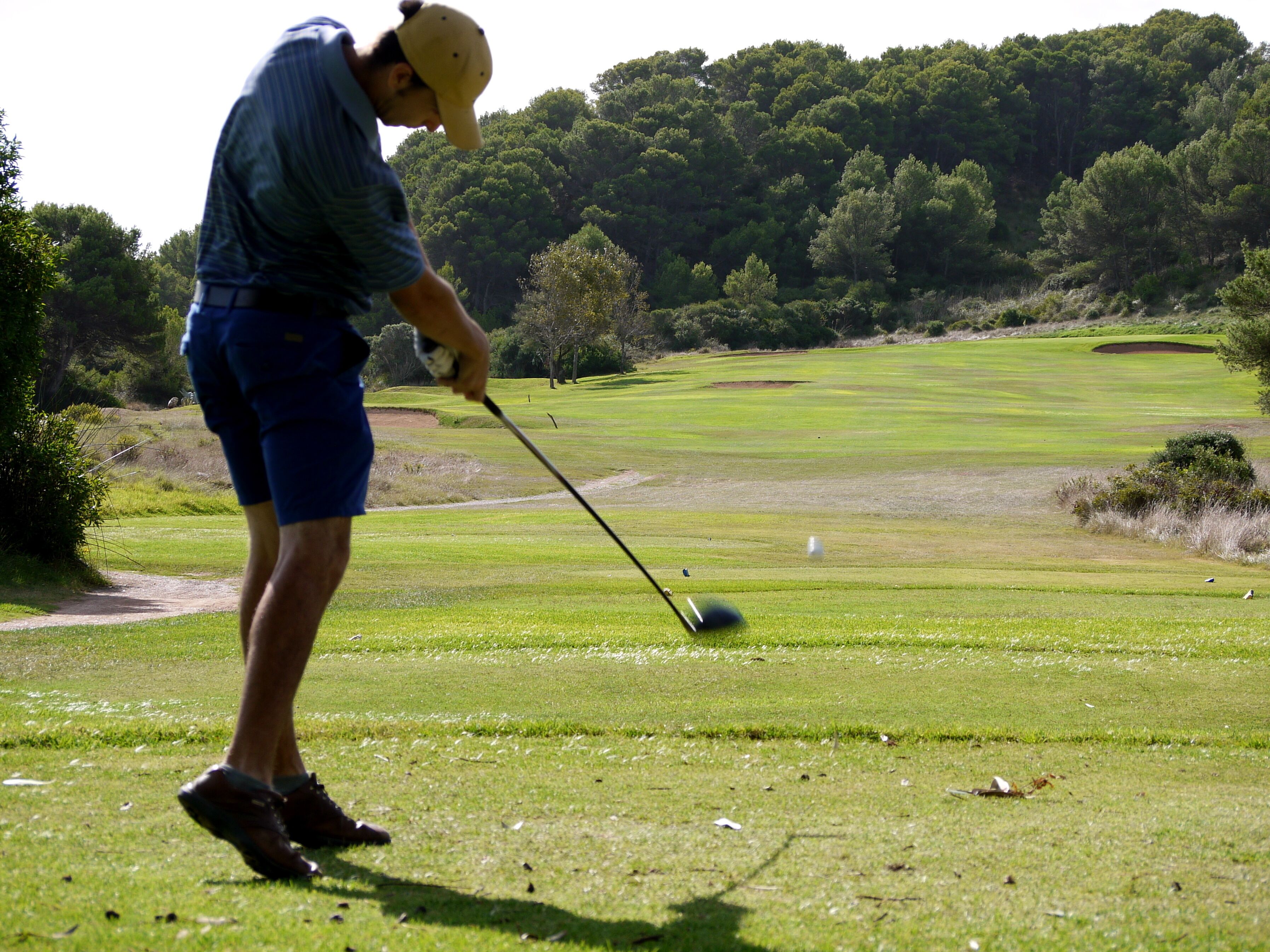Een persoon speelt golf op een verzorgde golfbaan met een bebost achtergrond.