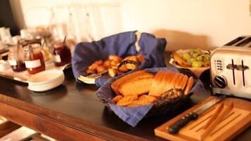 A buffet table with various food items, including bread, pastries, and a fruit bowl.