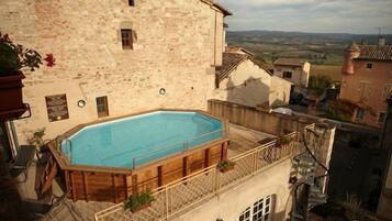 A stone building with a swimming pool on the second floor, surrounded by other buildings and a view of the countryside.