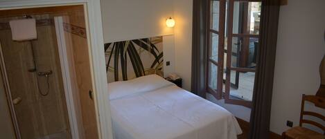 A hotel room with a bed, a shower, a chair, and a window with curtains.