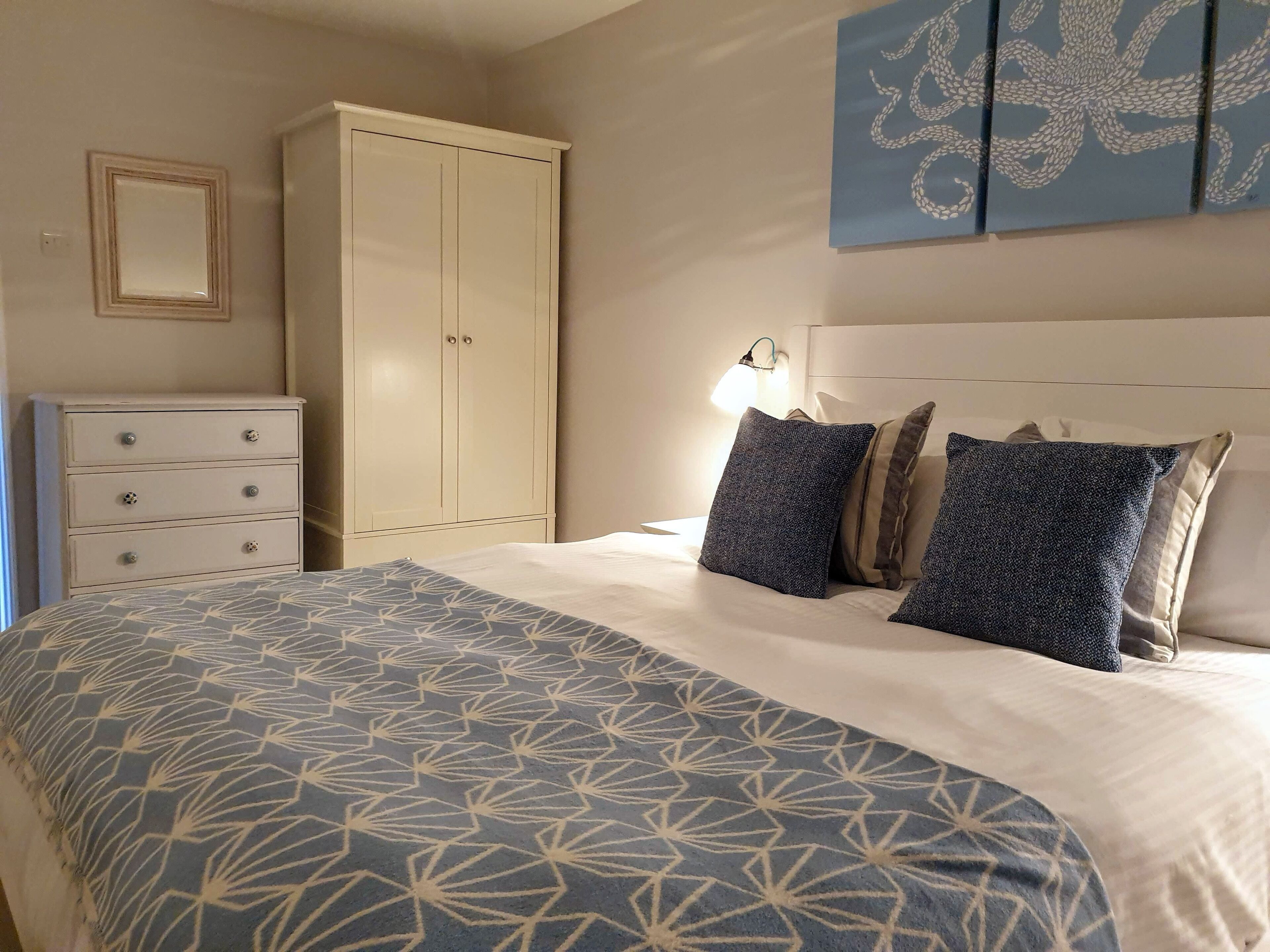 Un dormitorio con cama, armario, cómoda y lámpara fijada en la pared.