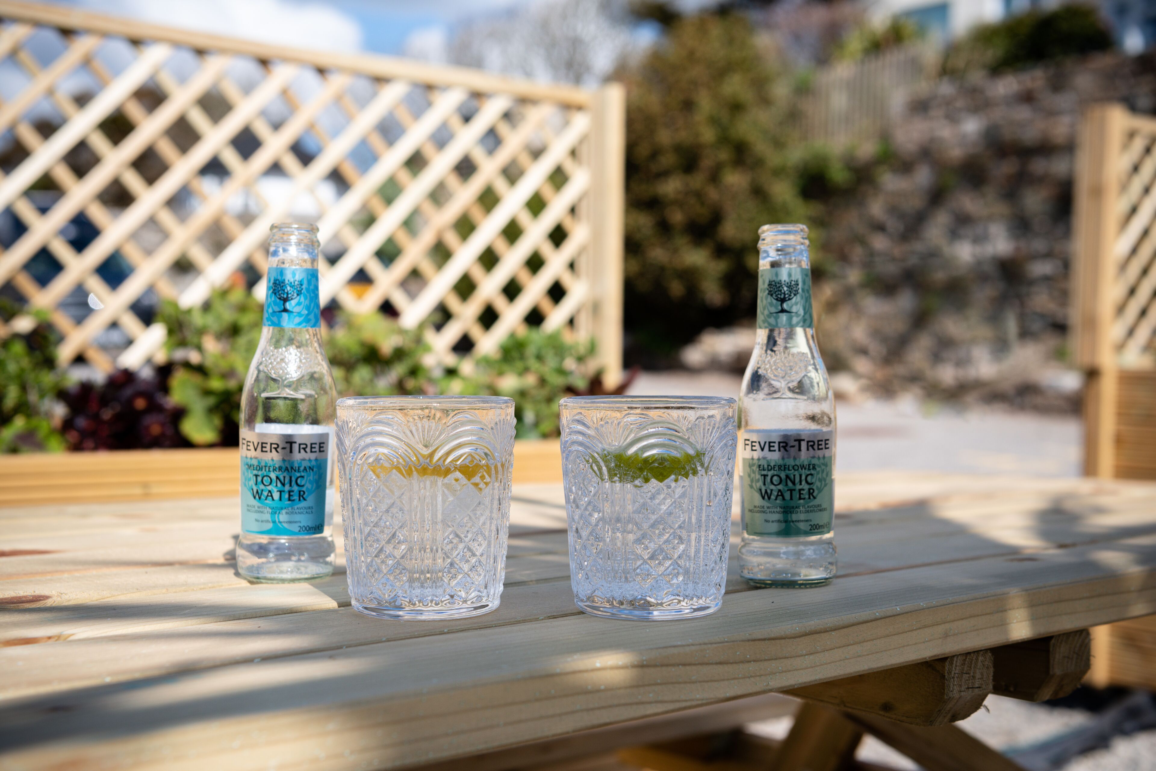 A wooden table with three bottles of tonic water and two glasses.