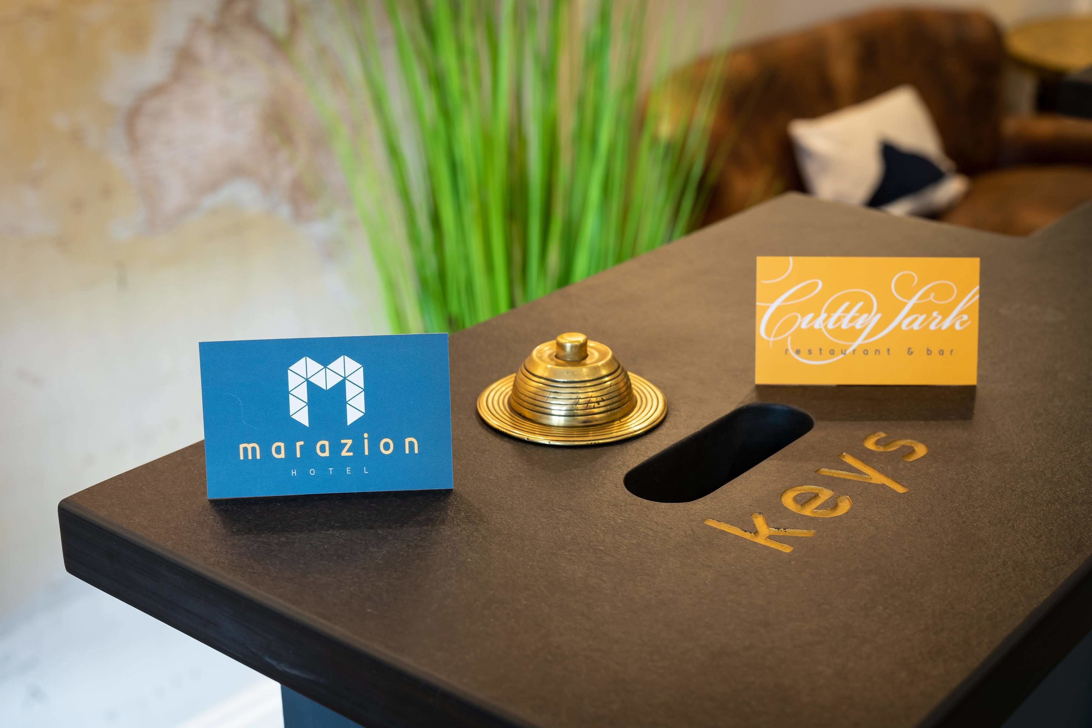 A hotel reception desk with a blue sign for 'Marazion Hotel' and a gold sign for 'Cottly Park Restaurant & Bar'.