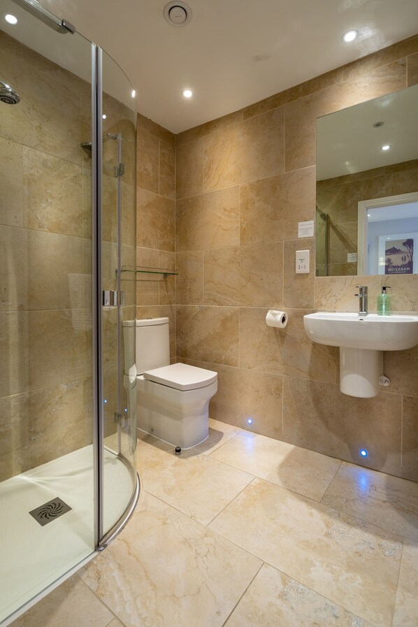 Un baño moderno con cabina de ducha de vidrio, inodoro y lavabo con espejo.