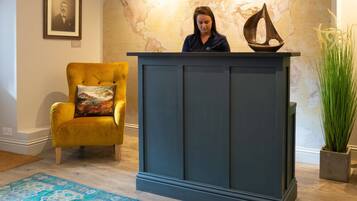 A room with a dark blue cabinet, a yellow armchair with a patterned cushion, and a large potted plant.
