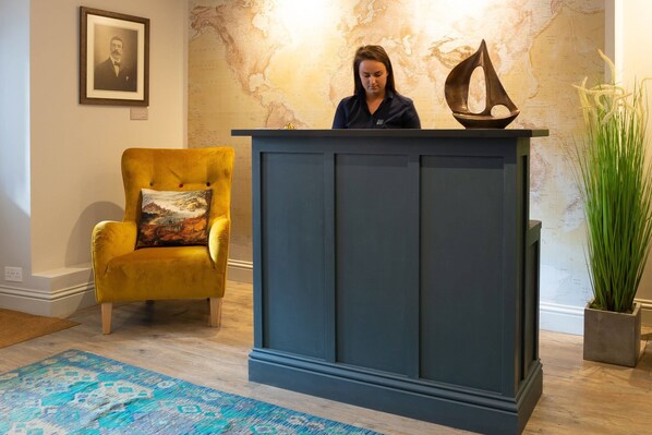 A room with a dark blue cabinet, a yellow armchair with a patterned cushion, and a large potted plant. - Marazion Hotel (Marazion)