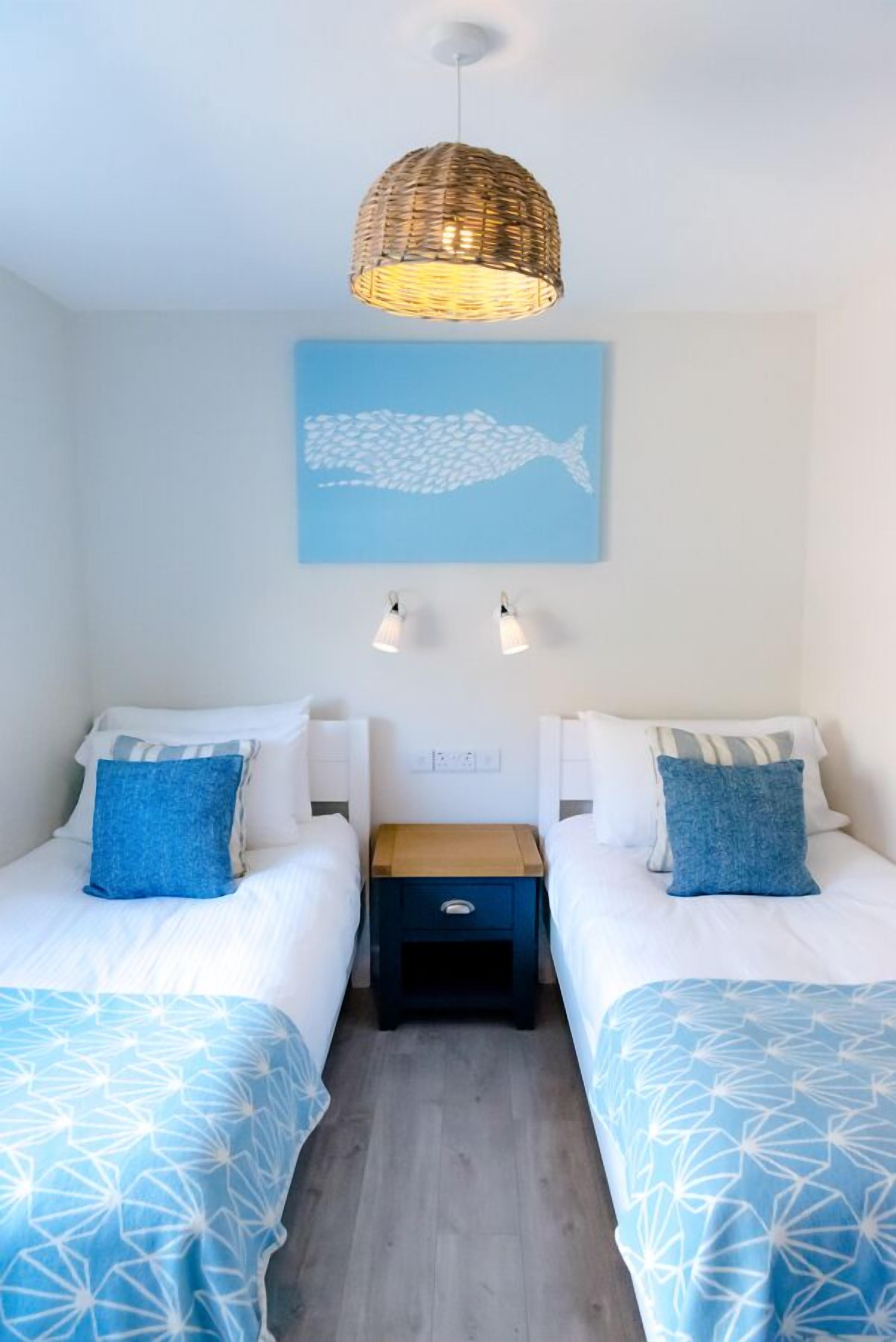 A room with two beds, each with a blue patterned bedspread, a wicker pendant light, and a wall-mounted light fixture.