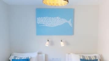 A room with two beds, each with a blue patterned bedspread, a wicker pendant light, and a wall-mounted light fixture.