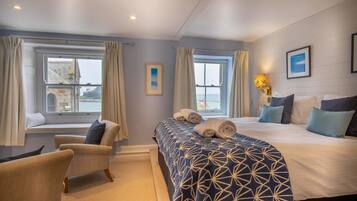 Habitación de hotel con una cama grande, dos sillones, una ventana con cortinas y vista al mar.